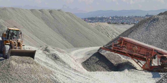 wheel loader excavator and mobile crusher against the background of crushed stone hills