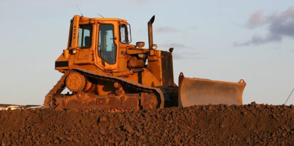 bucket of a bulldozer fills the trench with earth in an industrial zone