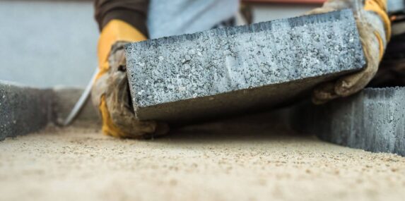 builder laying a paving brick placing it on the sand foundation
