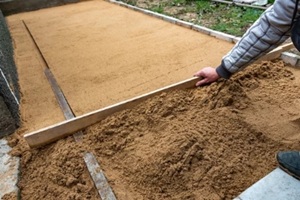 worker screening construction sand bedding to level for laying paving slabs in central florida