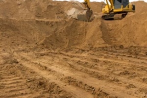 loader backhoe parked there on the mountain, which has a large pile of sand in the wheel tracks below