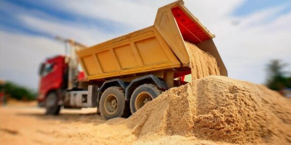 red and yellow dump truck is unloading a pile of sand on a Punta Gorda, FL construction site under a bright blue sky