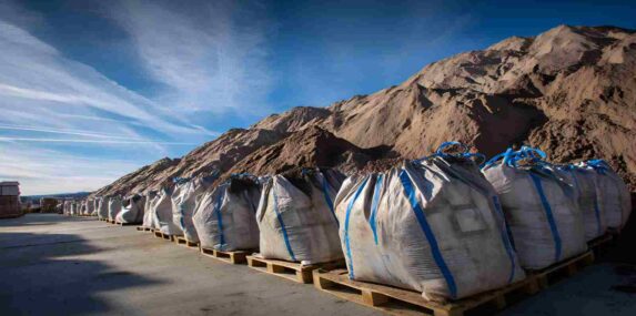Bags of Fill Dirt Placed on Pallets in Front of Large Pile