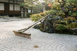 Wooden Rake Resting on Perfectly Patterned White Sand in A Garden