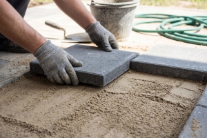 Professional Worker Laying Grey Stone Pavers on Prepared Sand Foundation Outdoors